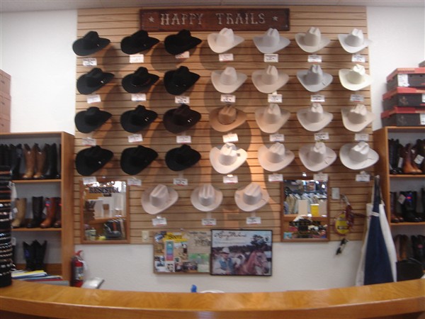 Display wall of black and straw cowboy hats under a Happy Trails sign