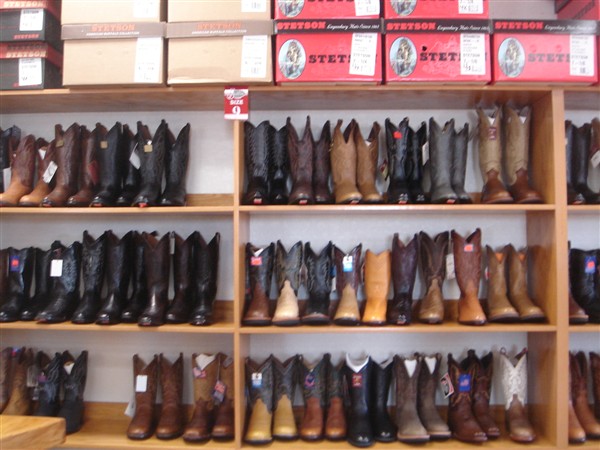 Wall of western boots on wooden shelves beneath stacked Stetson boxes